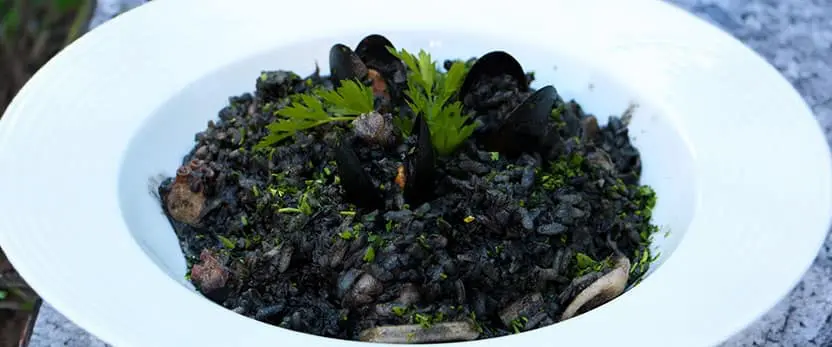 se muestra el platillo Risotto al nero al frutti di mare